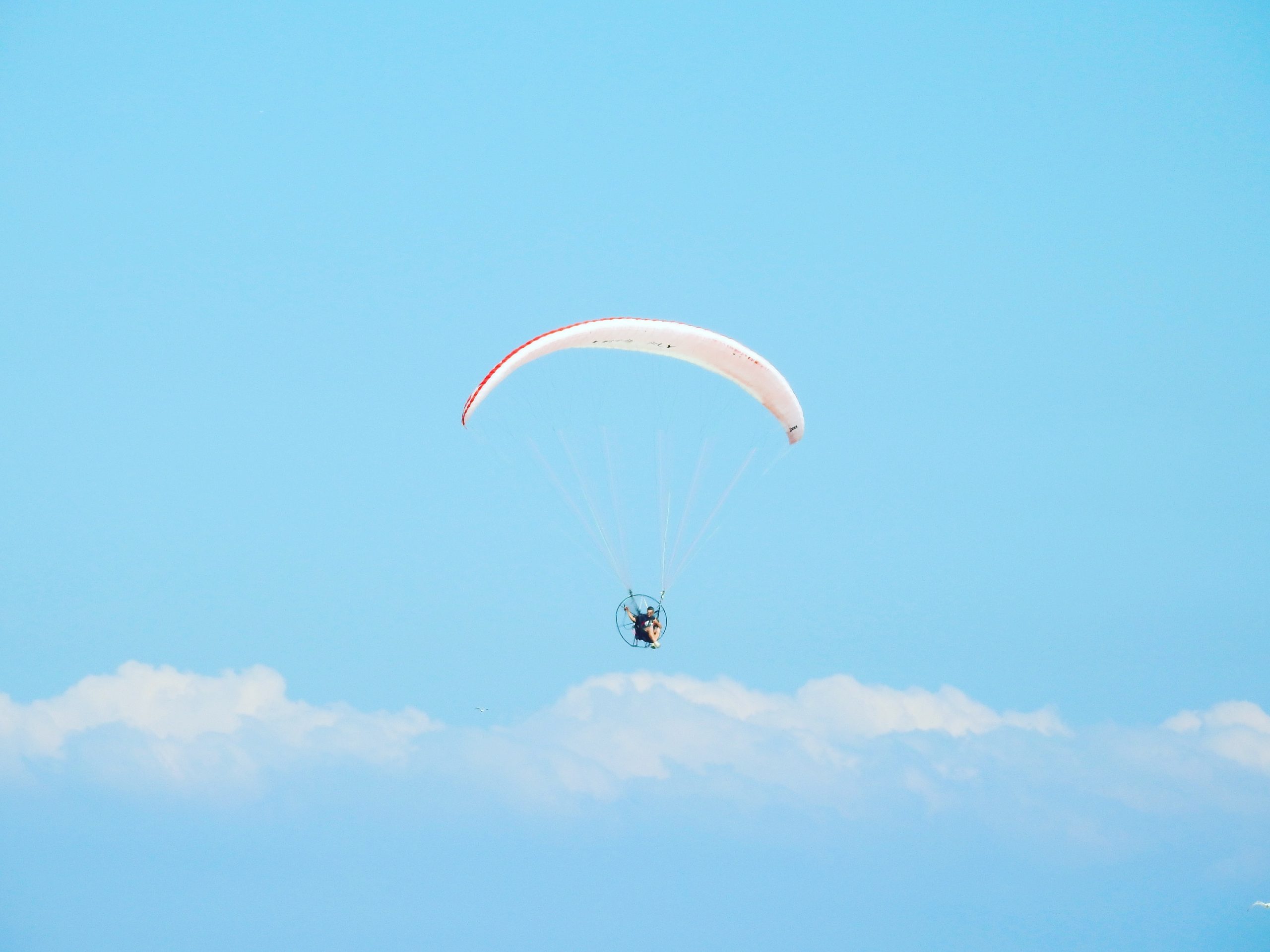 A low angle shot of a person parachuting down under the beautiful cloudy sky